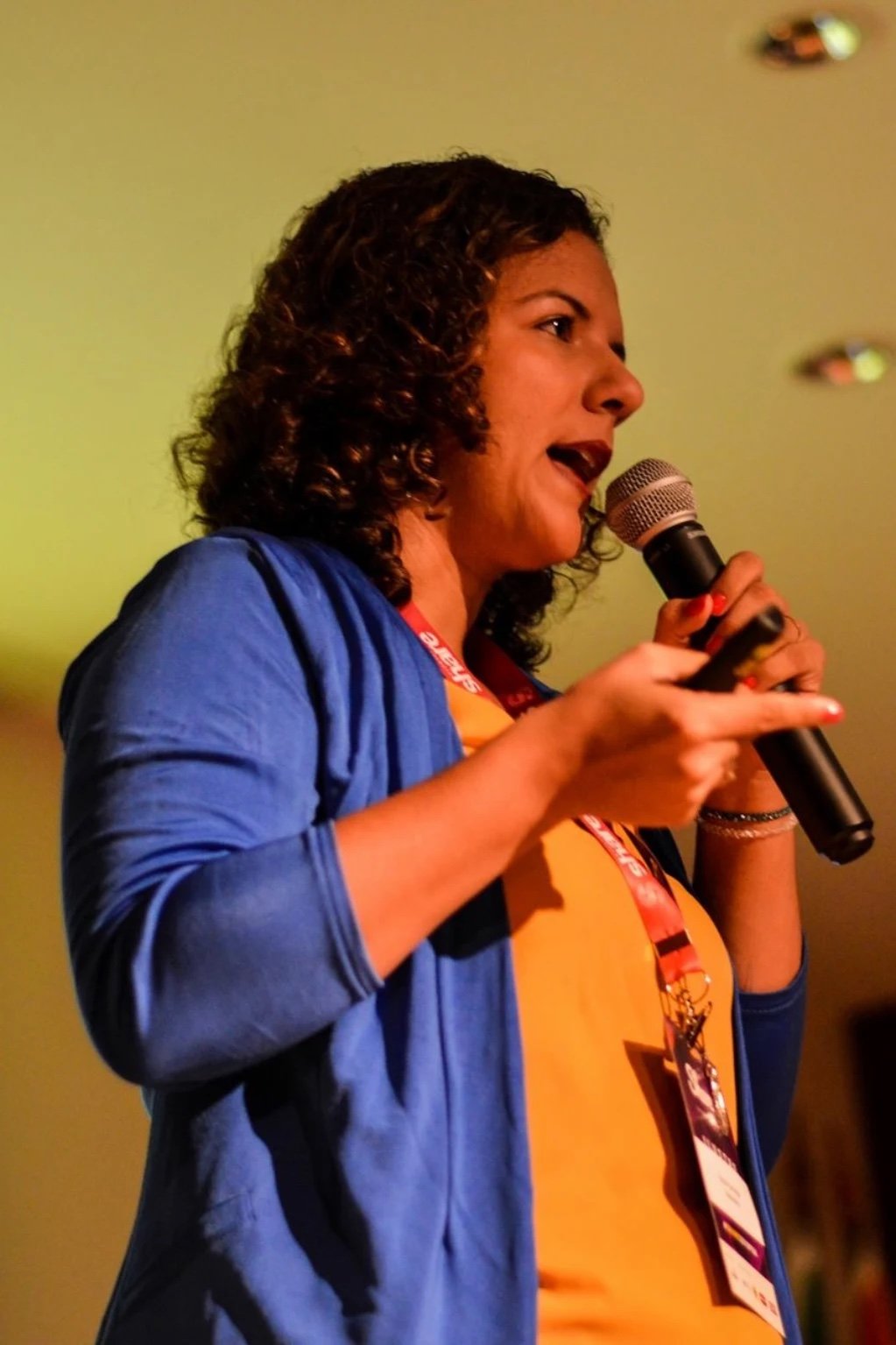 Raquel Camargo speaking on stage with a microphone at a conference